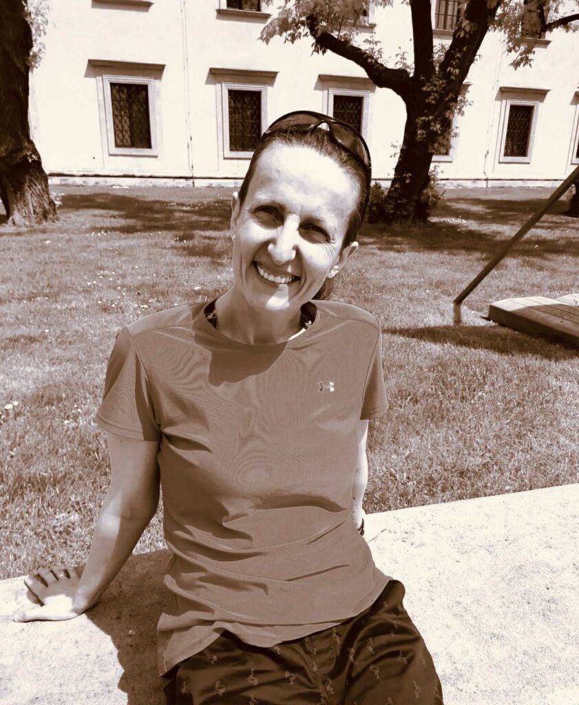 Uśmiechnięta Izabela Wlizło w swobodnym stroju siedząca na murku